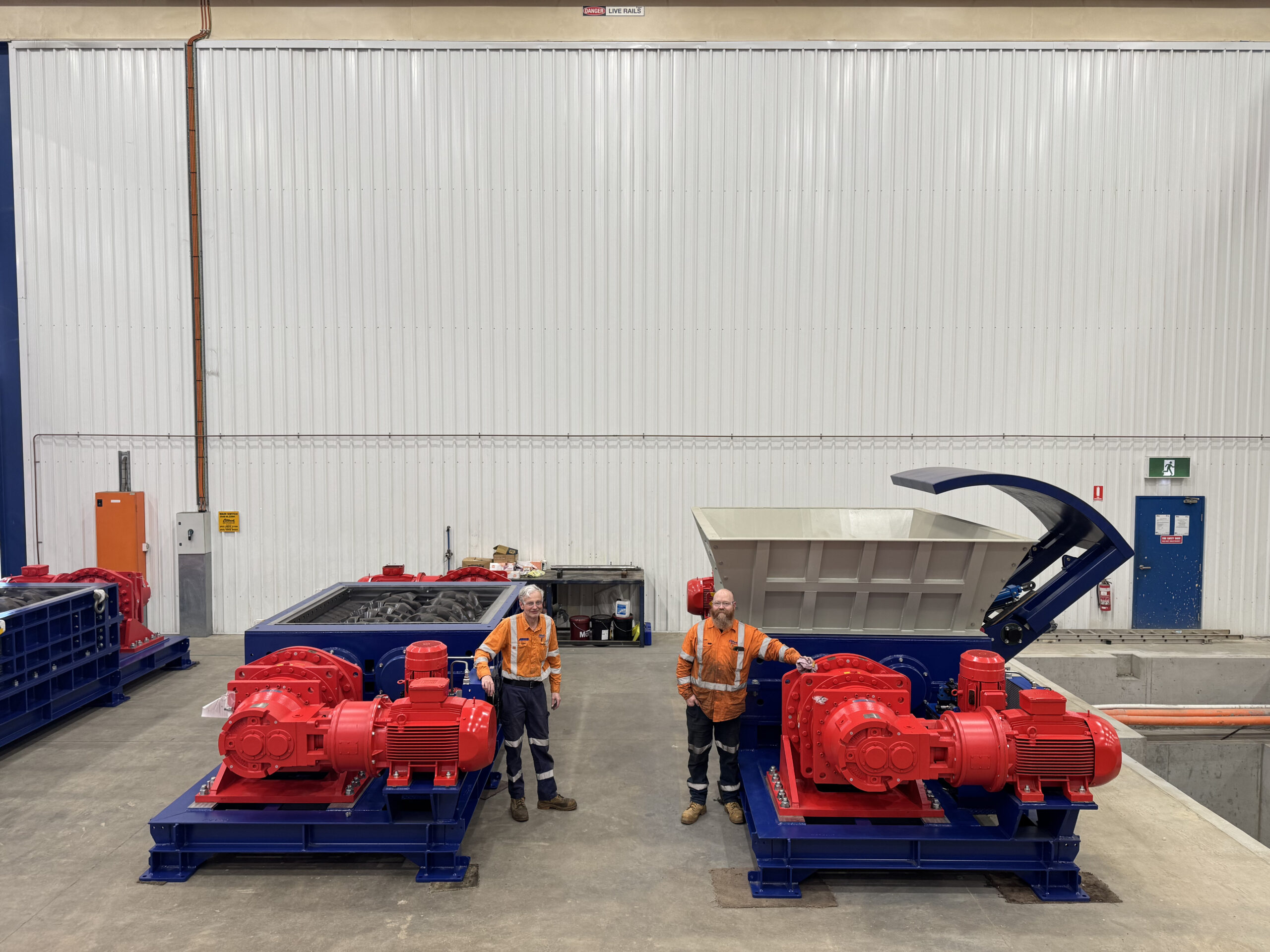 Two Eilbeck workers stand beside two blue shredders with red drives in the workshop