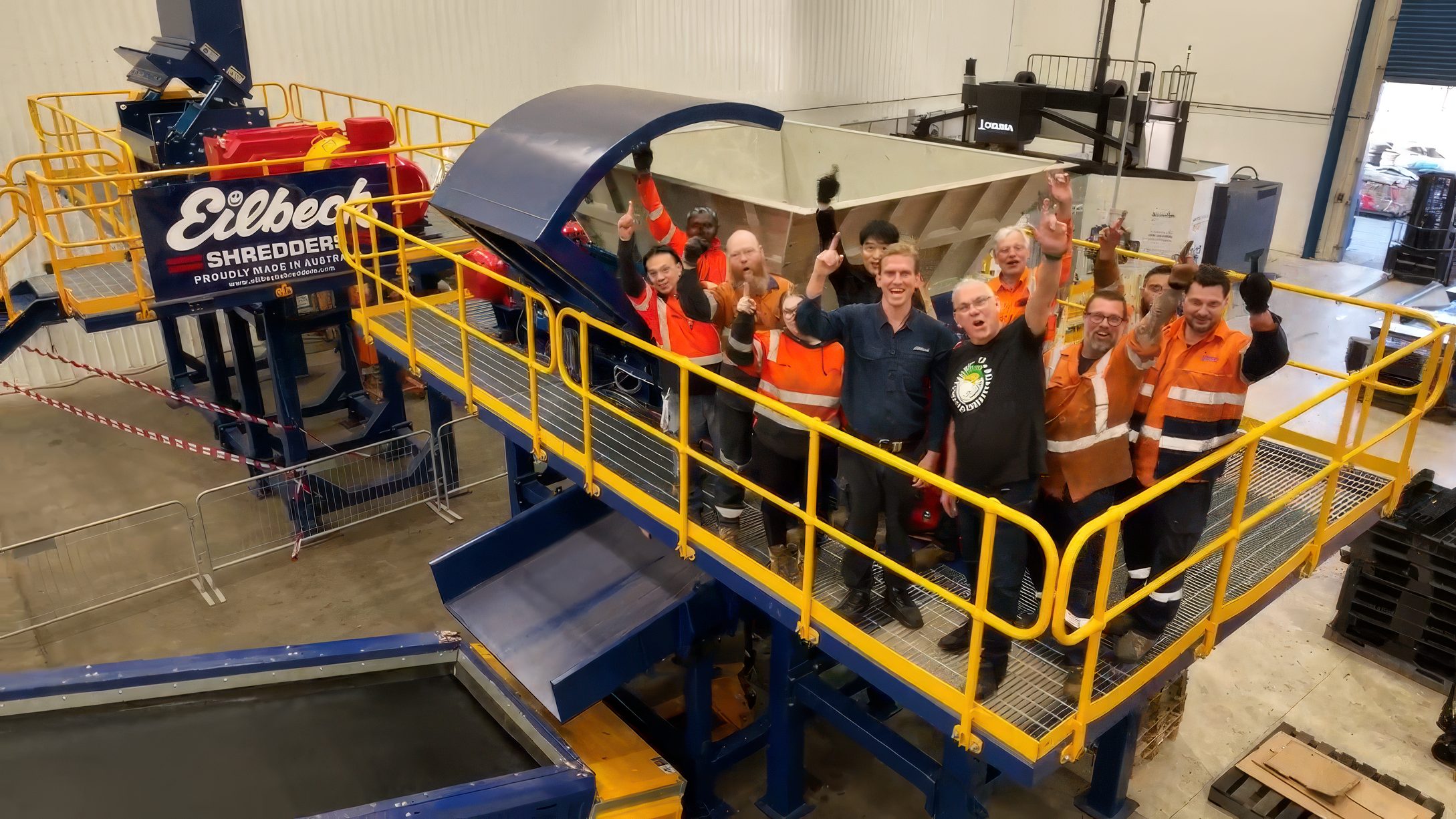 Eilbeck staff stand on the walkway of a finished shredder and raise their hands