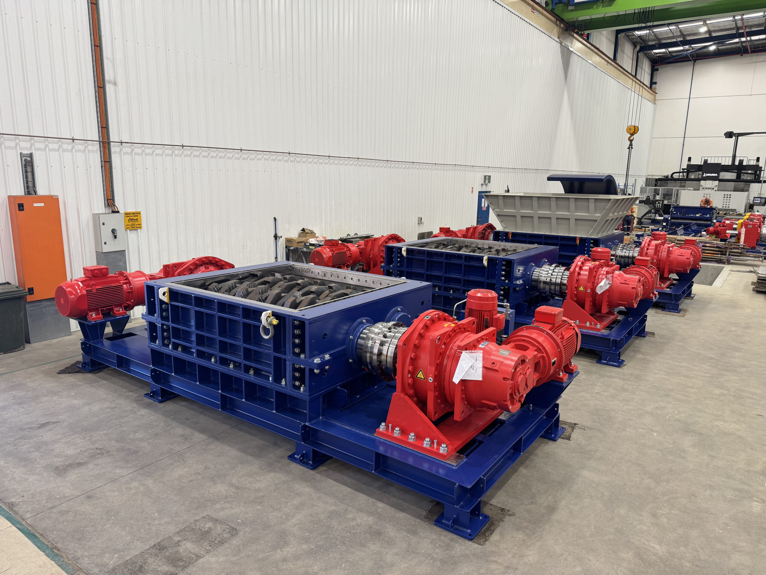 Two blue dual-shaft shredders with red gearboxes and motors on the workshop floor