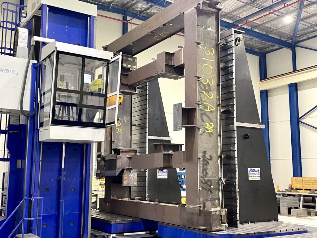 A large fabricated steel frame on the bed of a machining centre, with the operator cab beside it