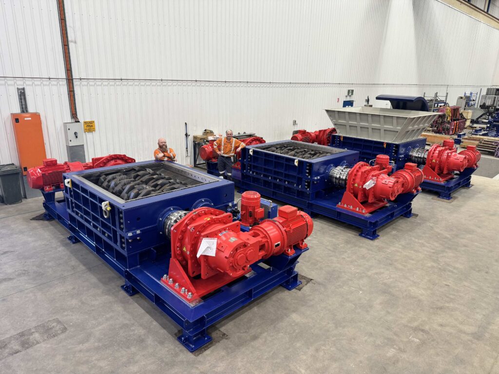 Three Eilbeck dual-shaft shredders with red drives on the workshop floor, two of the team behind them
