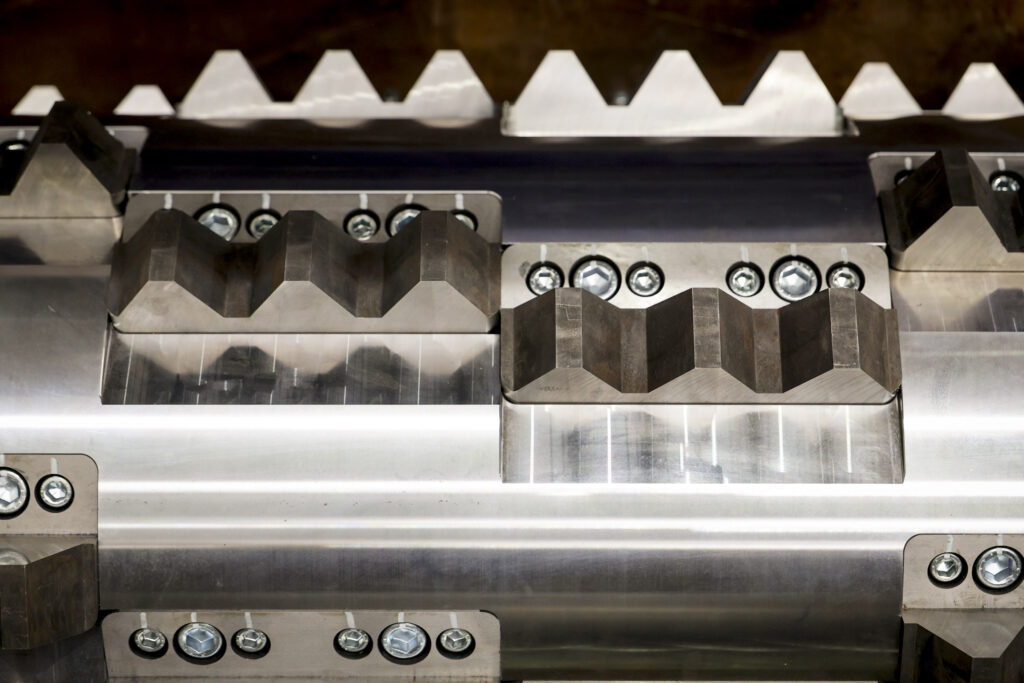 Close-up of a rasper rotor, its bolted V-shaped knives set in staggered rows below a row of counter knives
